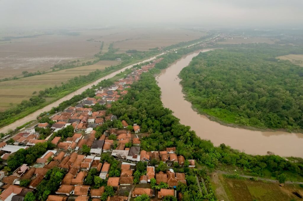 Aerial view of a lush village landscape nestled beside a winding river on a cloudy day.